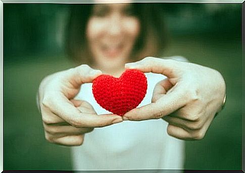 Woman holds a small red, knitted heart in her hands as she stretches out in front of her hands