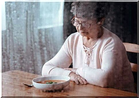 An elderly woman who is upset and looking at a plate of food.