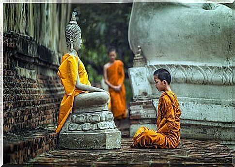 A boy sitting in front of a statue of Buddha and practicing a type of Buddhism